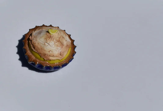 Small lemon meringue pie in a blue bottle cap on a light gray background