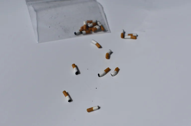 Handmade miniature cigarette butts scattered on a white surface with a clear plastic bag in the corner.