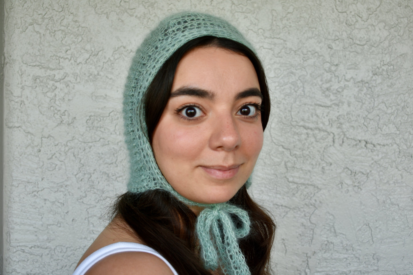 Woman wearing a light green crochet silk mohair bonnet against a plain background