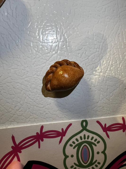 Miniature handmade empanada magnet on a textured white refrigerator.