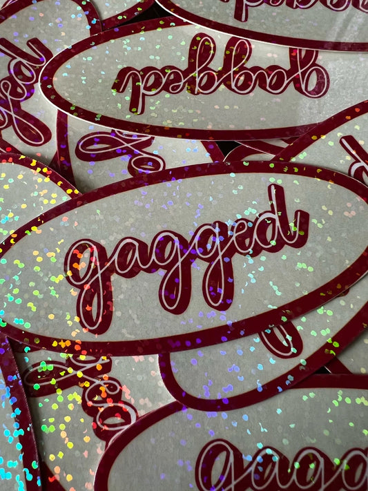Sticker with 'gagged' text in cursive on a gray background with colorful confetti.