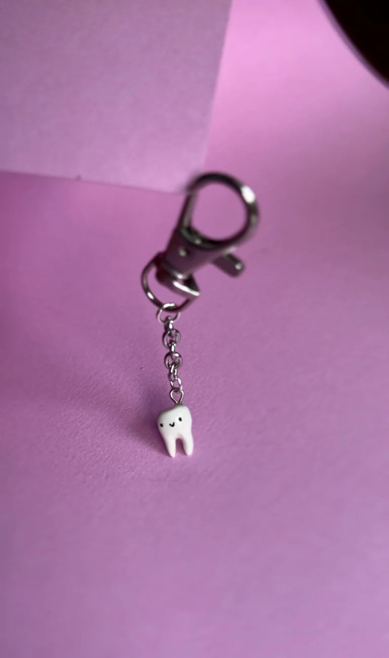 Keychain with a tooth-shaped charm on a pink background