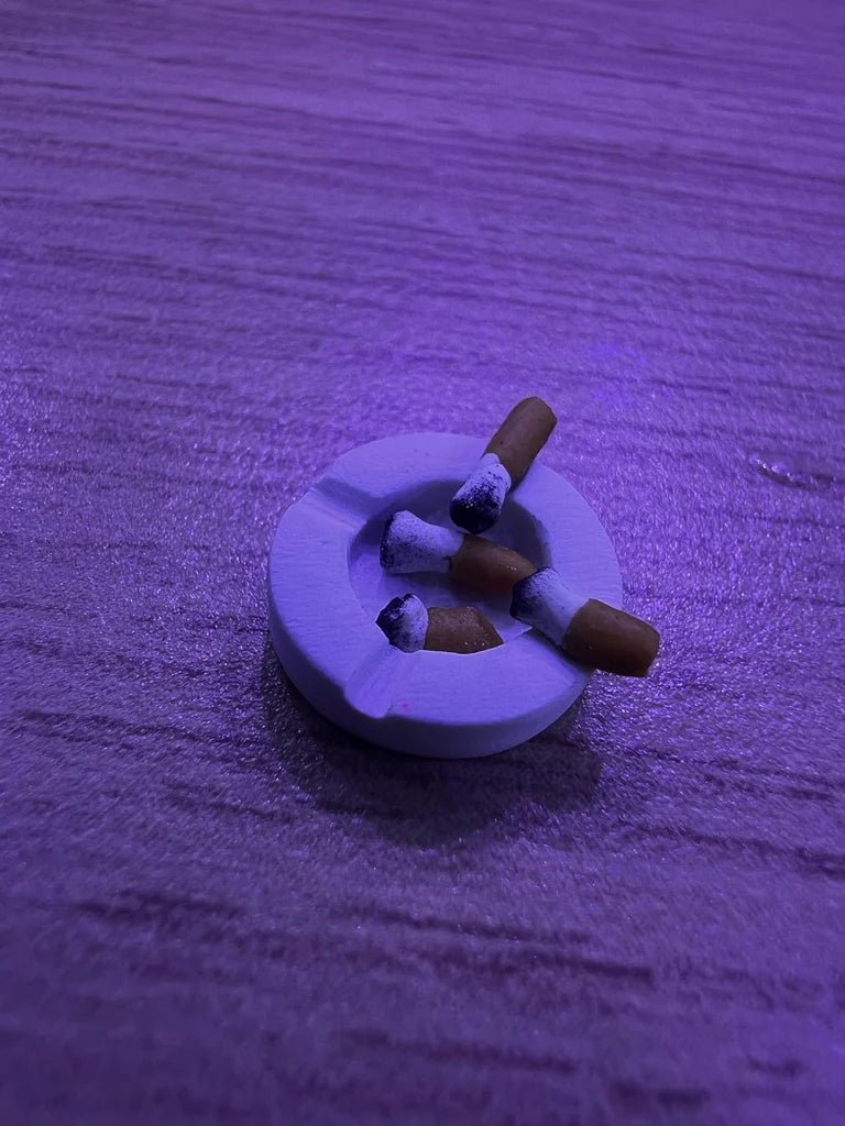 White ashtray with cigarette butts on a textured purple surface