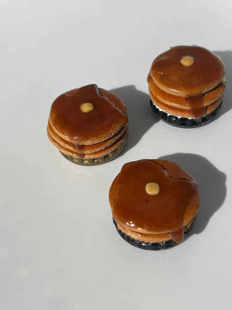 Three miniature brown stacks of pancakes with a yellow cube placed center on a white surface