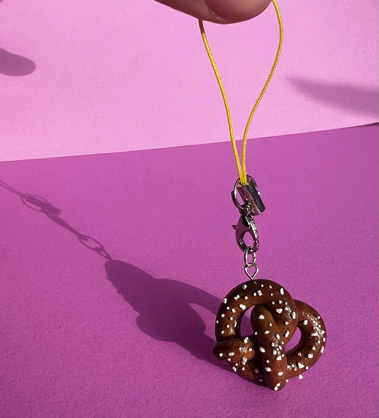 Pretzel-shaped keychain on a yellow string against a pink background