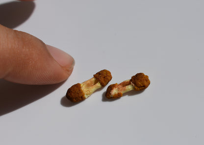 Two small miniature friend chicken wings next to a finger for comparison size, on a white background.