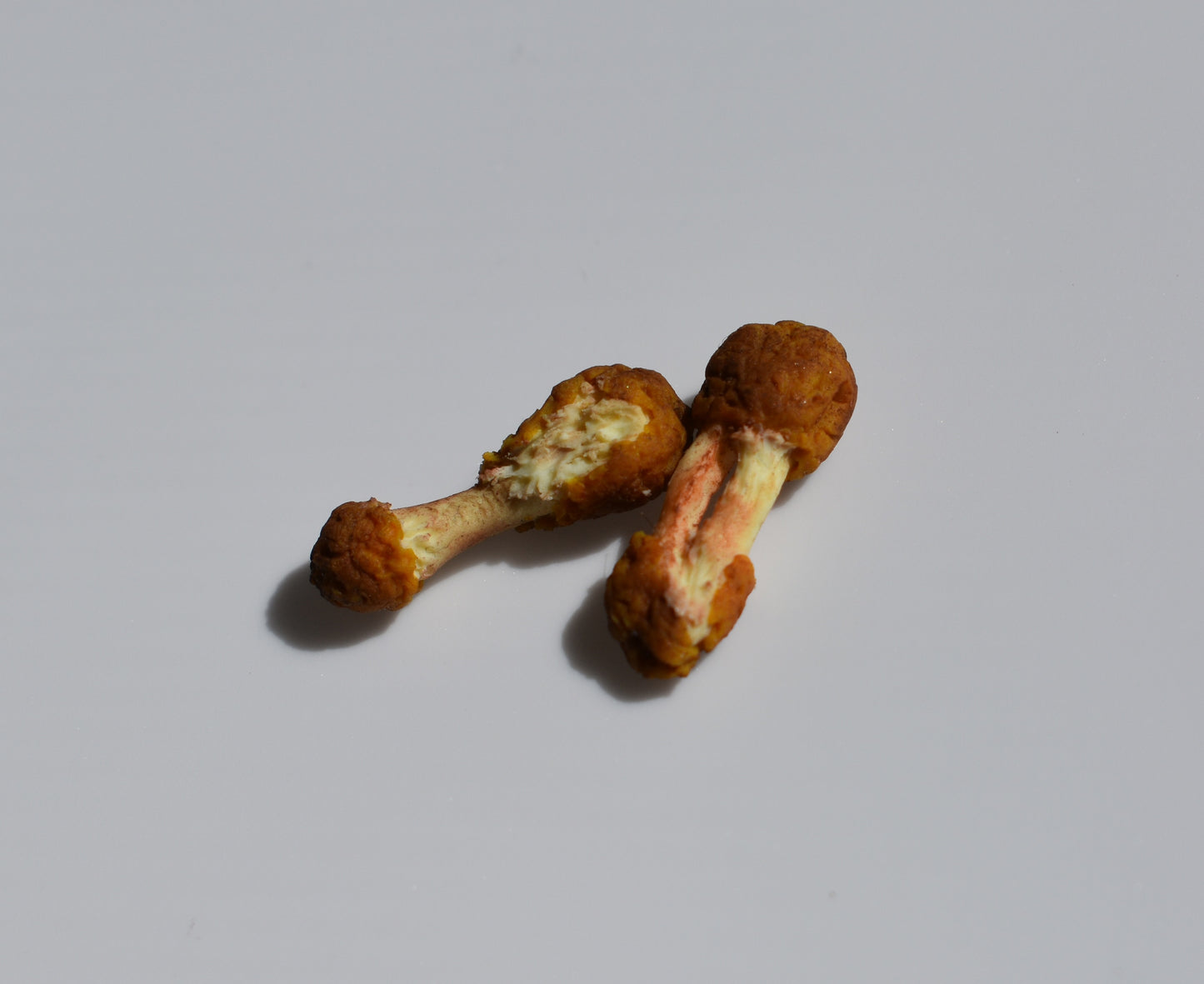 Two miniature friend chicken drumsticks sit on a white background.