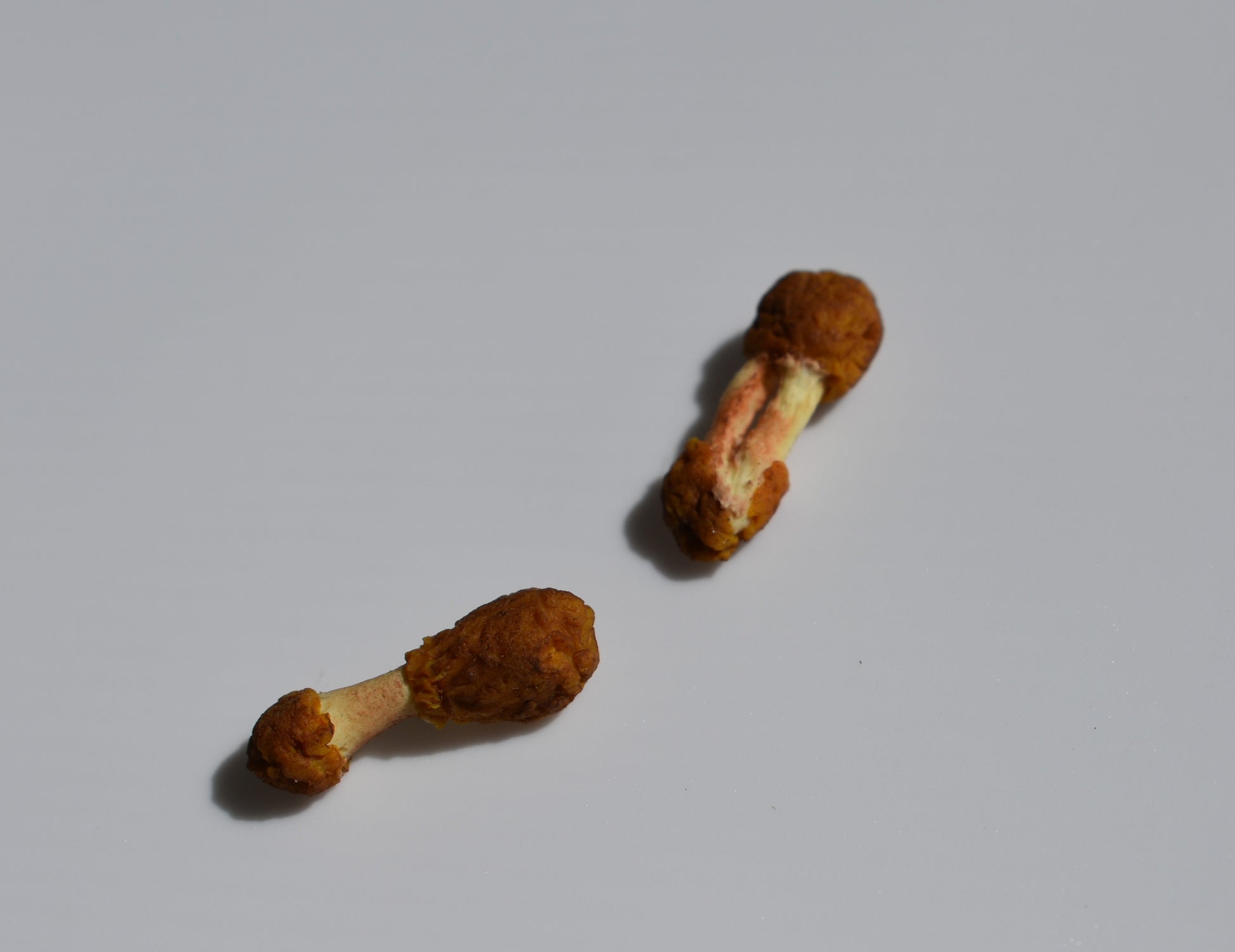 Two miniature fried chicken wings. One is a drumstick and one is a flat sit on a white background. Both are eaten and feature fried remnants and bone.