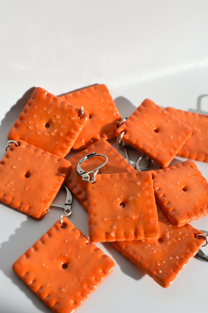 Orange square-shaped cheddar cracker looking crochet markers on a white background