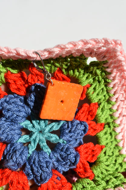 Colorful crocheted fabric with a square crochet marker made to look like a cheddar cracker. There is a floral pattern on a white background