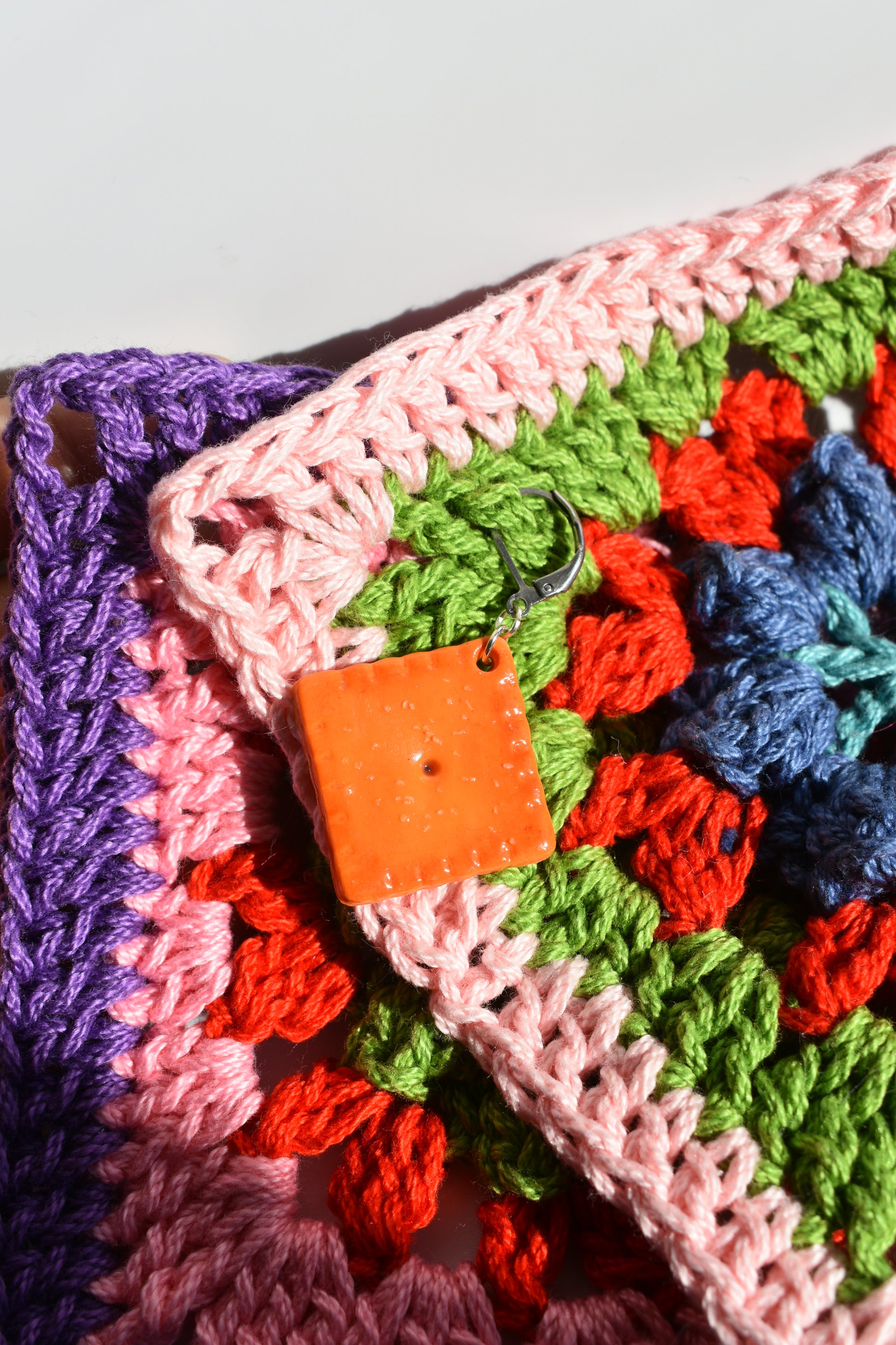 Colorful crocheted fabric with a crochet marker made to look like a cheddar cracker attached with a white background.