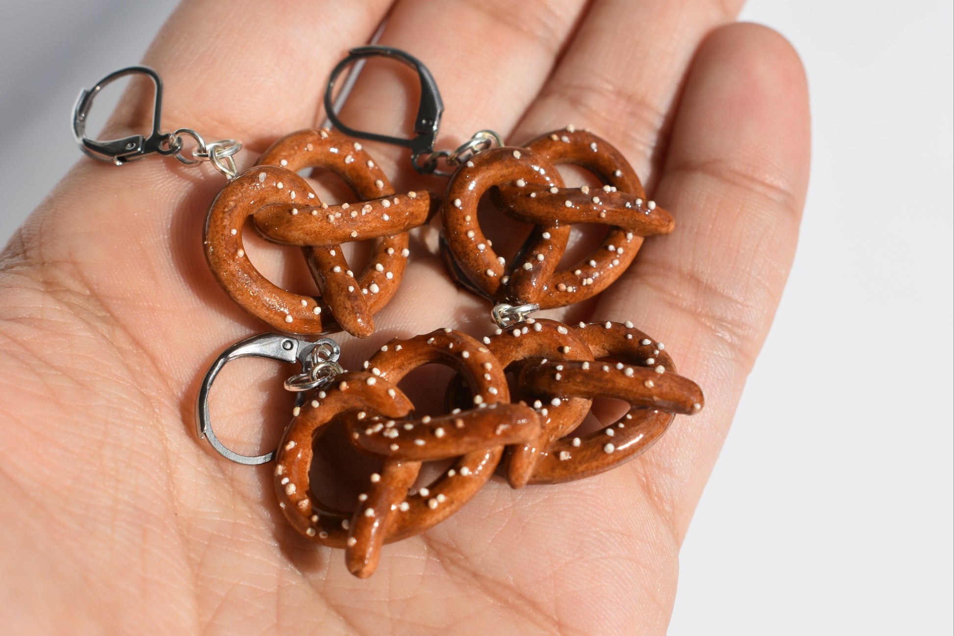 Hand holding four mini pretzel-shaped keychains against a neutral background