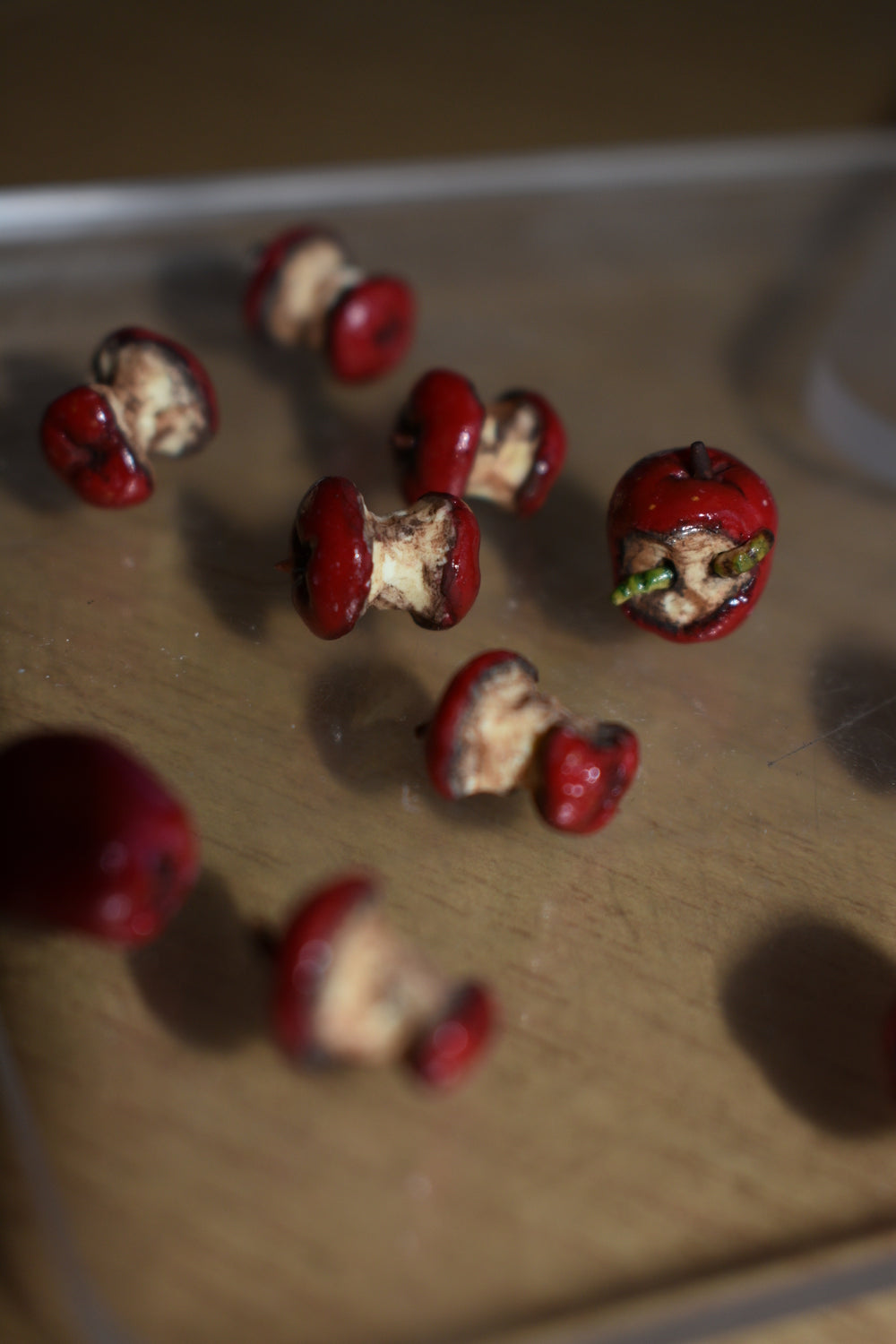 miniature red apple cores. One apple core has two green slimy worms making their way out of the center of the oxidized apple.