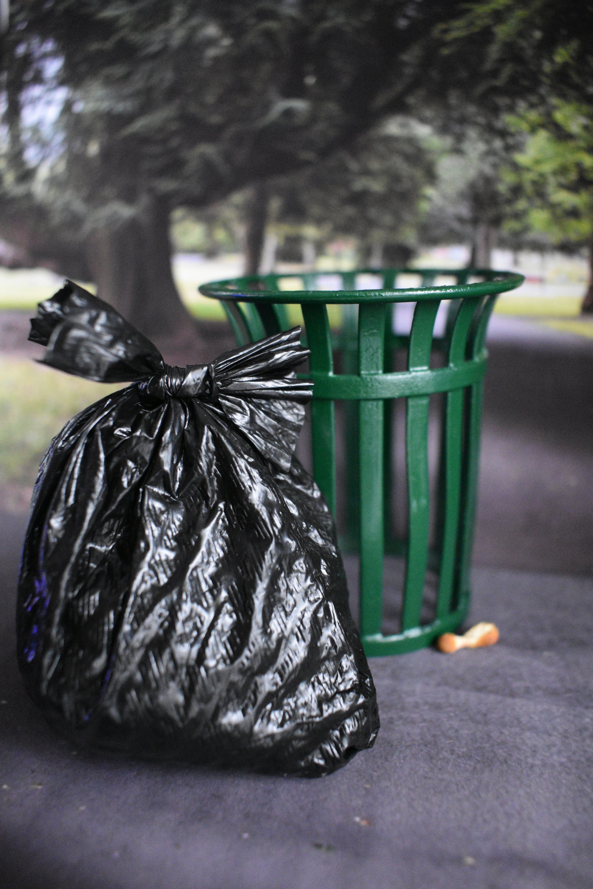 Black trash bag tied to a green trash can in a park setting