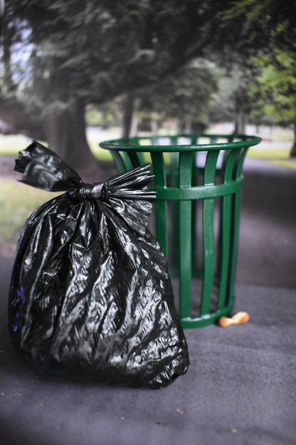 Black trash bag tied to a green trash can in a park setting