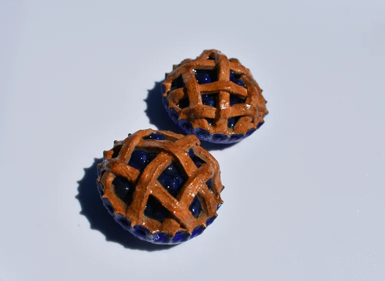 Pair of miniature blueberry pie magnets on a white background. 