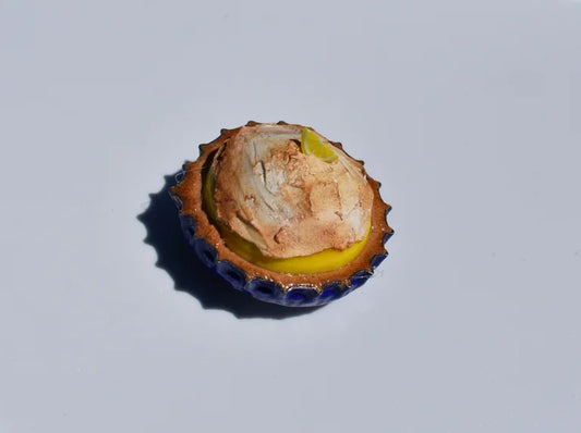 Close-up of a bottle cap with a lemon meringue pie inside on a light gray background