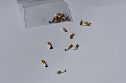 Handmade miniature cigarette butts scattered on a white surface with a clear plastic bag in the corner.