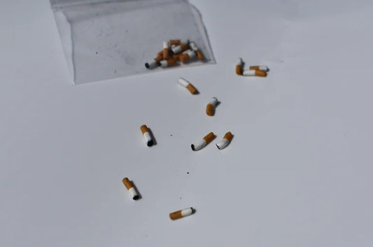 Handmade miniature cigarette butts scattered on a white surface with a clear plastic bag in the corner.