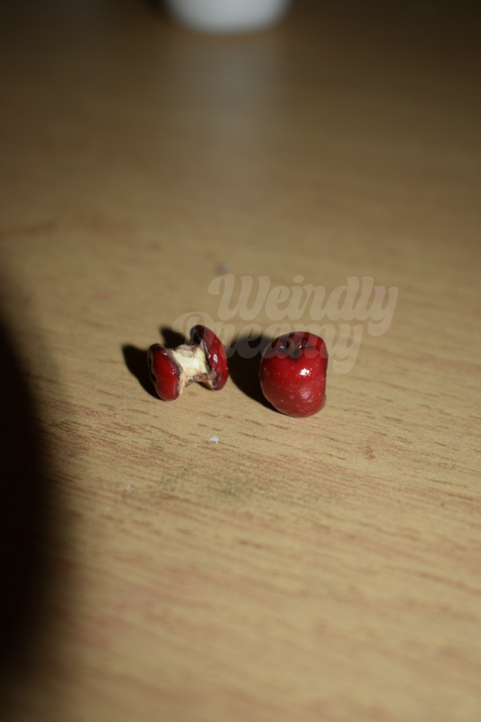 Two red miniature apples on a wooden surface with a blurred background. There is an apple core to the left and a solid red apple to the right.