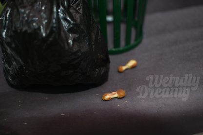 Two chicken wing bones on a dark surface next to a black trash bag.