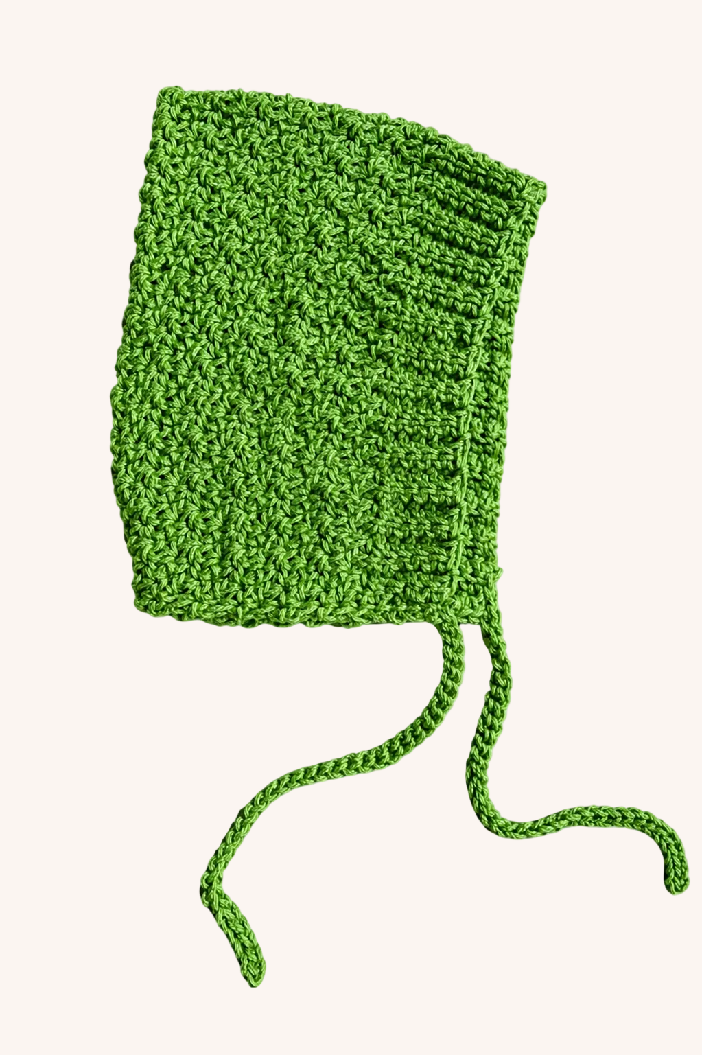 Kelly green crochet baby bonnet resting on a beige background with two tassles hanging below