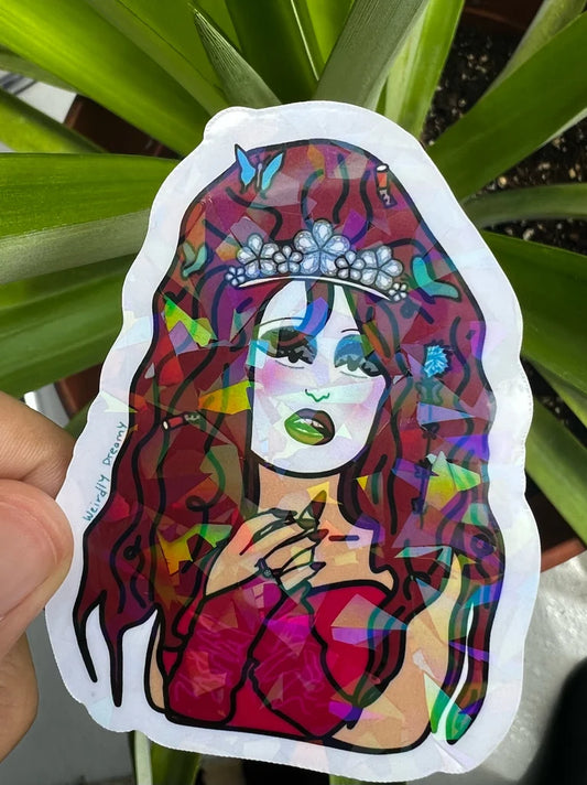 Colorful sticker of a woman with a tiara held in front of green leaves.