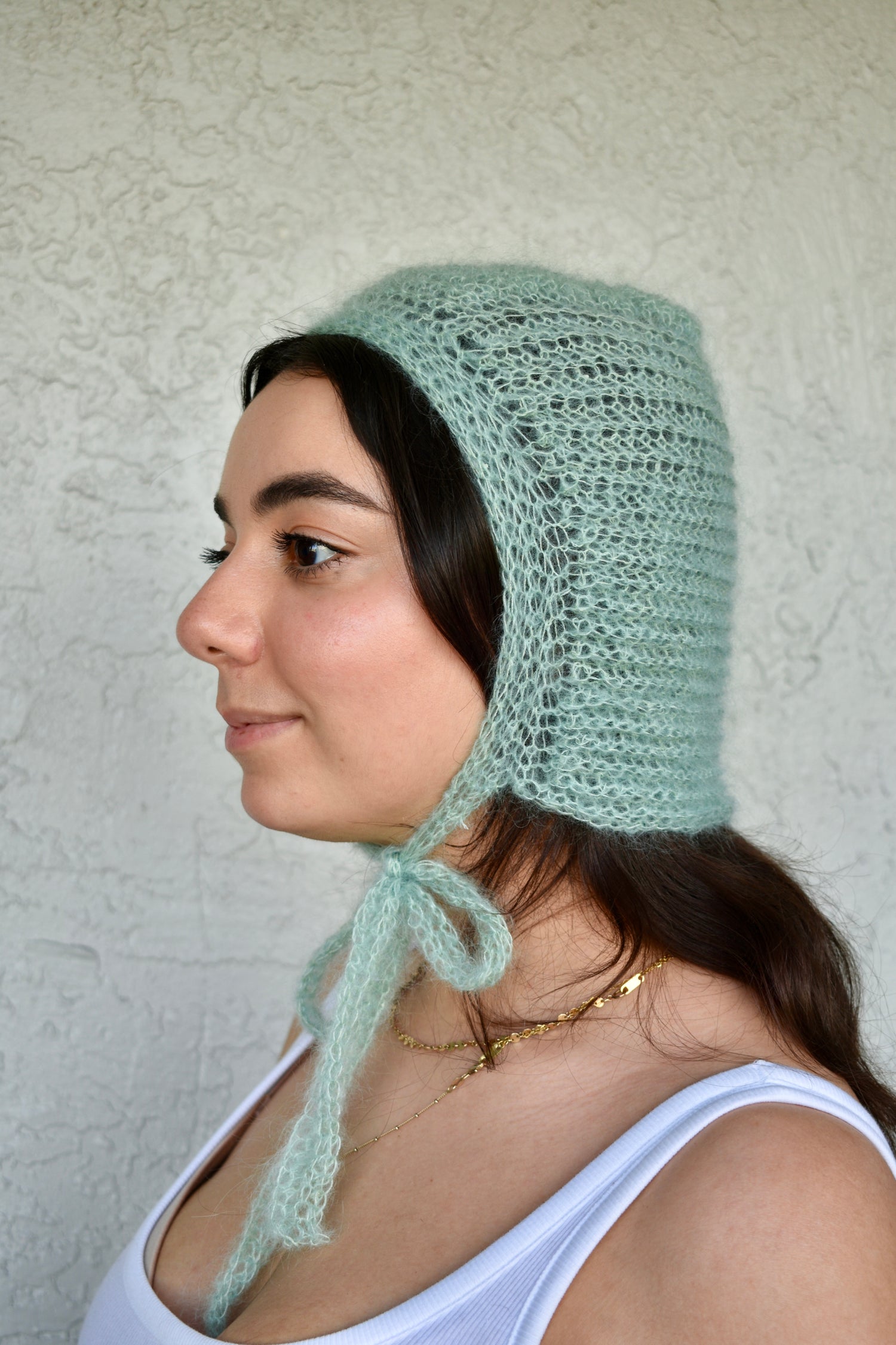 Woman wearing a light green knitted bonnet against a textured white background