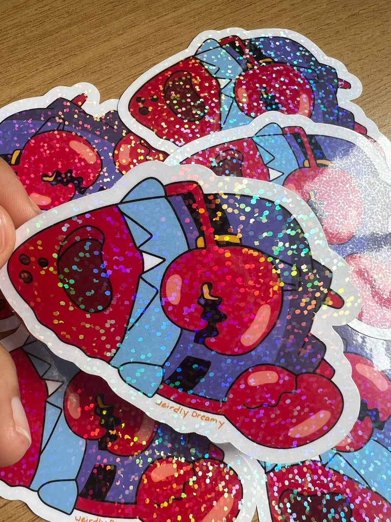 Colorful glittery sticker with cartoon character held by a hand on a wooden surface