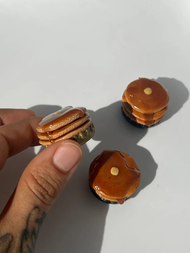 Miniature food models of a layered stack of pancakes held by a hand on a white background