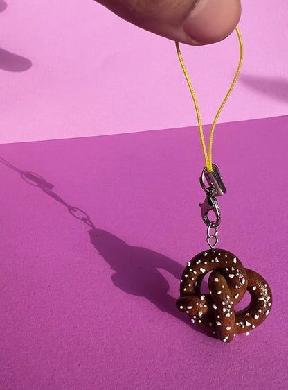 Brown pretzel-shaped keychain on a yellow string against a pink background