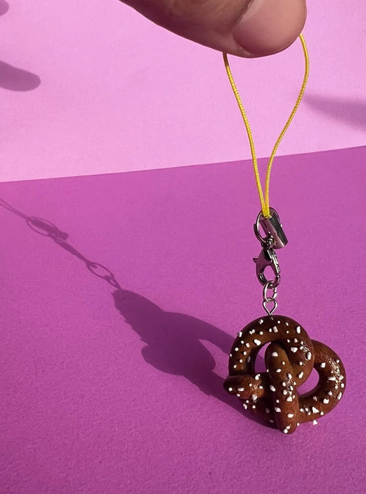 Brown pretzel-shaped keychain on a yellow string against a pink background