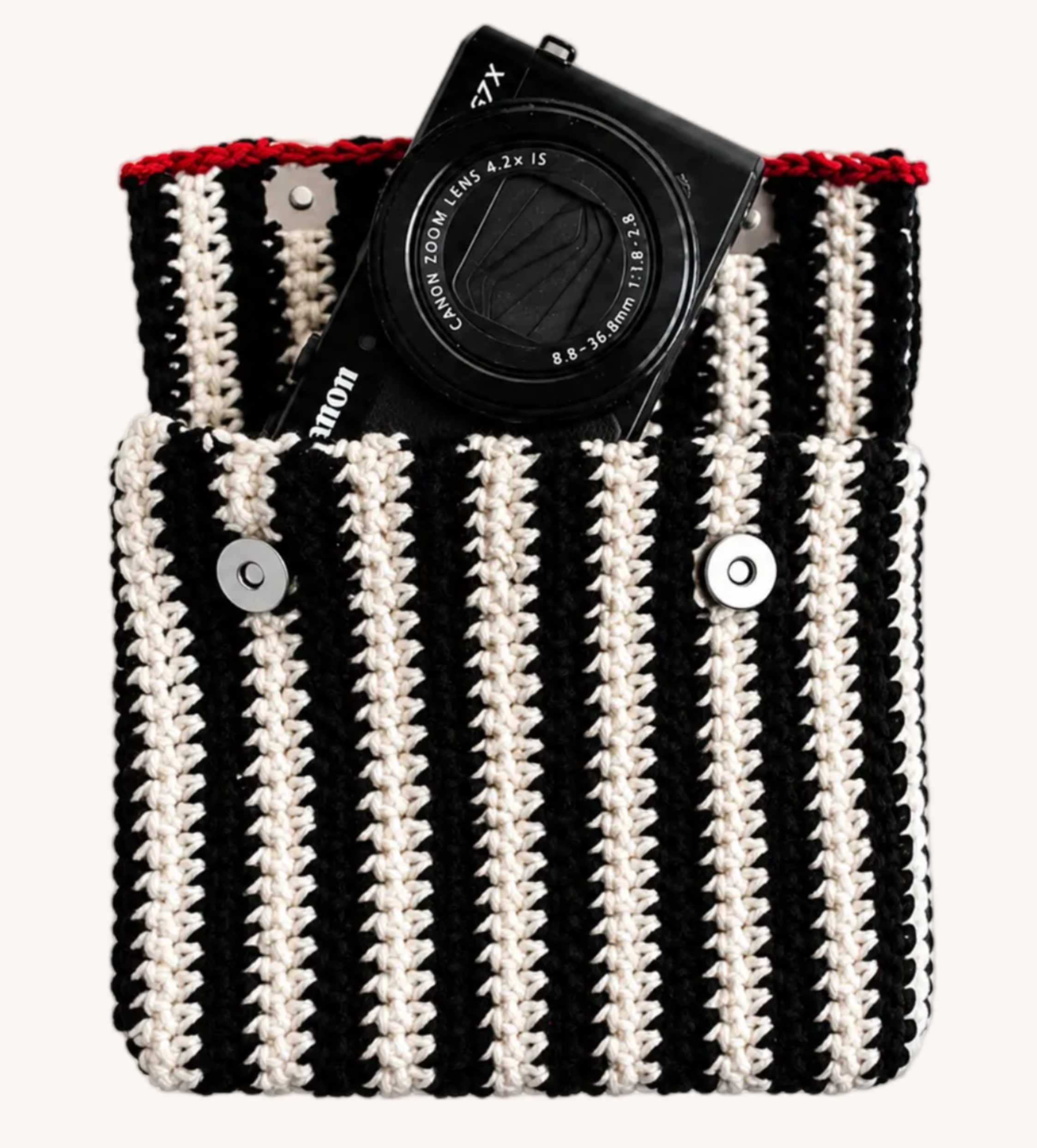 black and beige striped pouch with red trimming. Two magnetic claps are visible, and there is a camera poking out of the pouch.